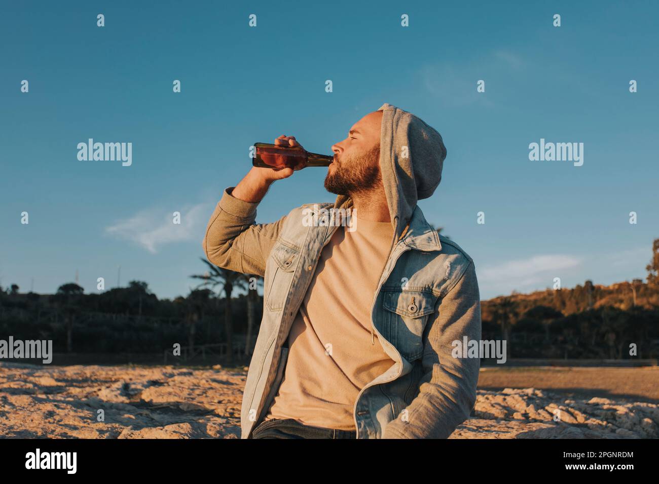 Man drinking beer at sunset under sky Stock Photo