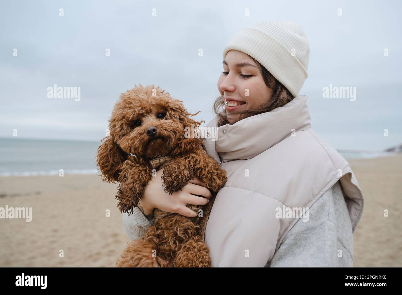 Happy woman holding Maltipoo dog at beach Stock Photo