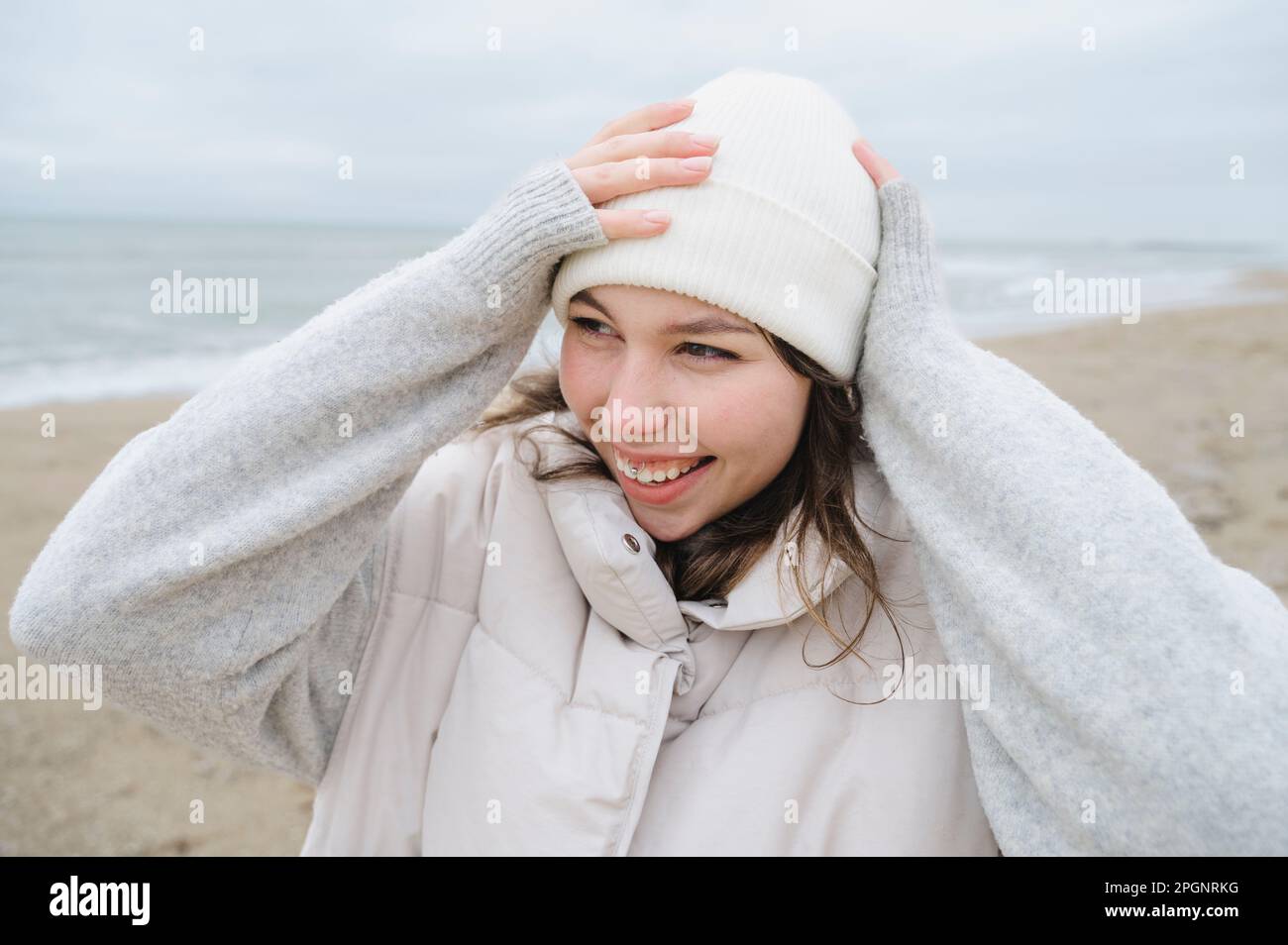 Happy woman adjusting knit hat at beach Stock Photo