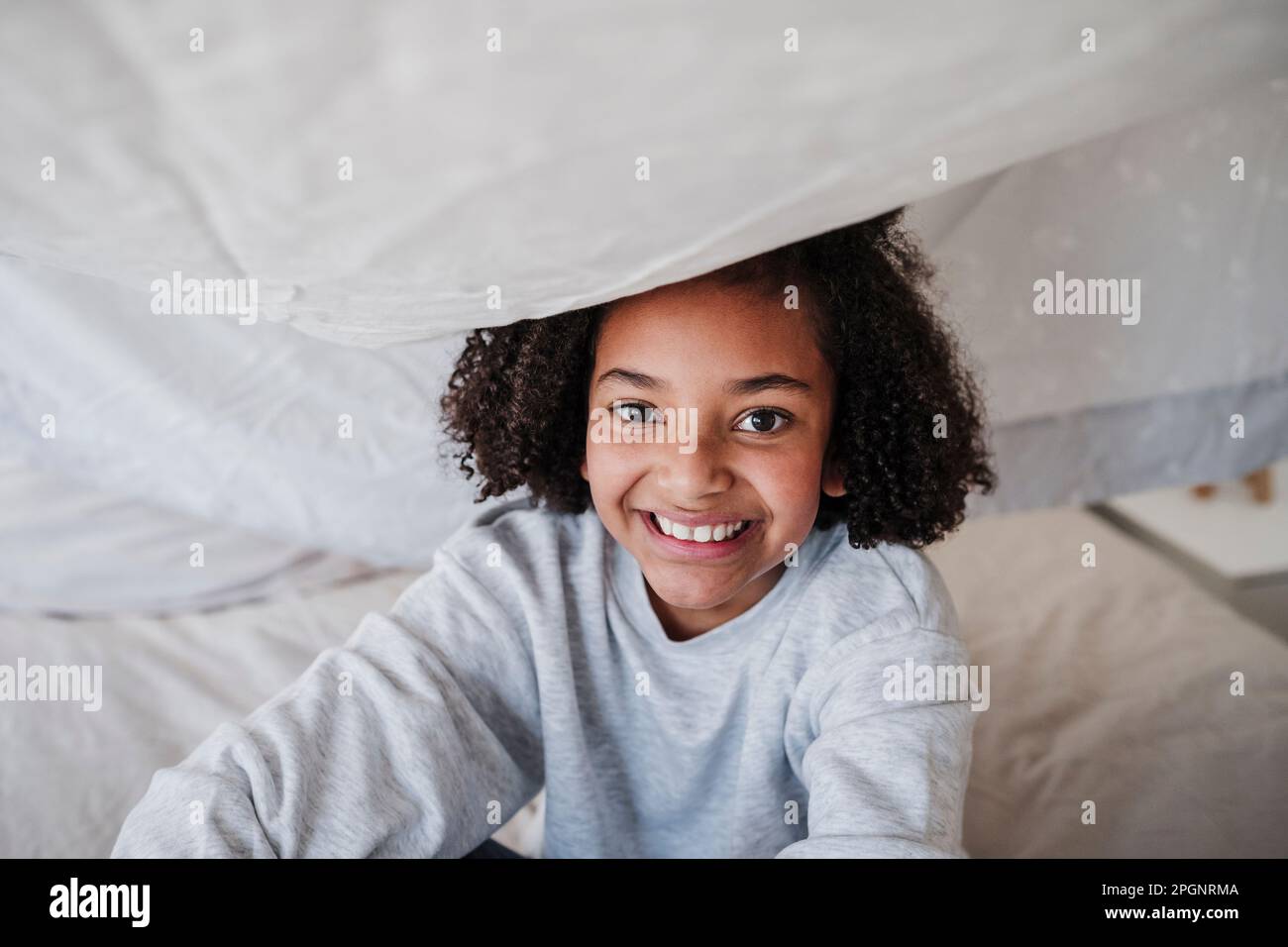 Happy girl sitting on bed under blanket at home Stock Photo Alamy