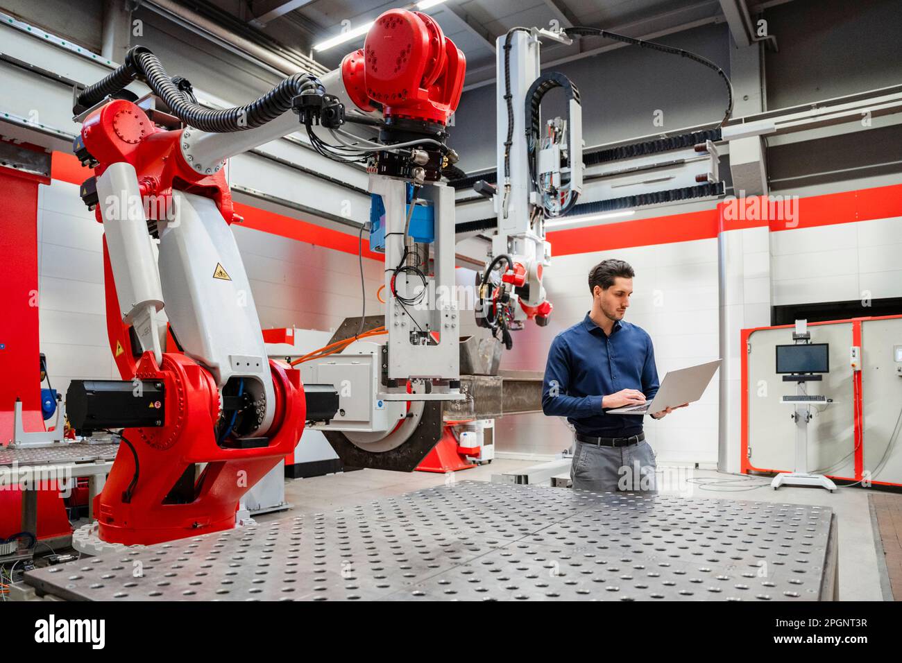 Engineer using laptop standing in robot factory Stock Photo