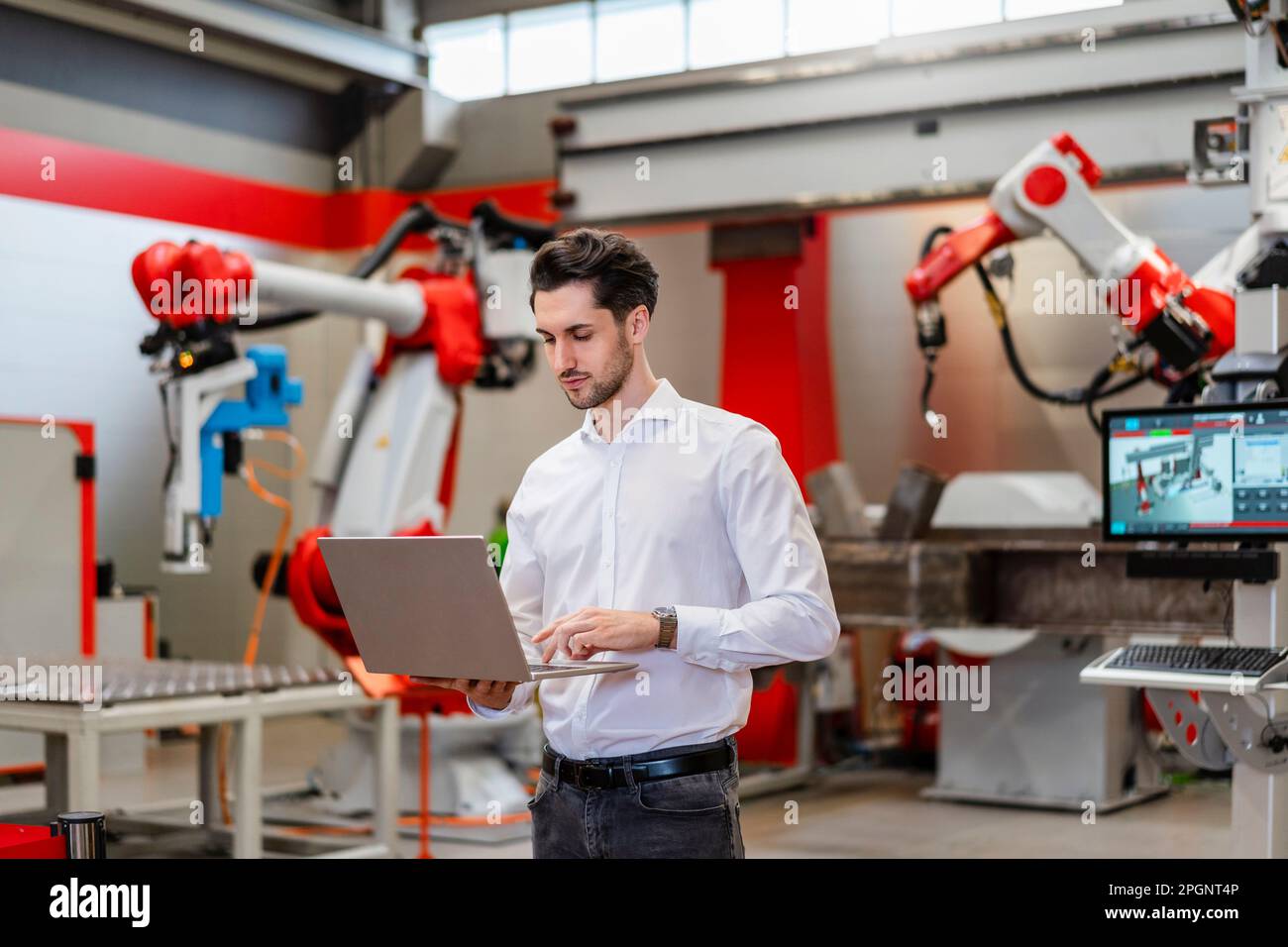 Engineer using laptop standing in robot factory Stock Photo