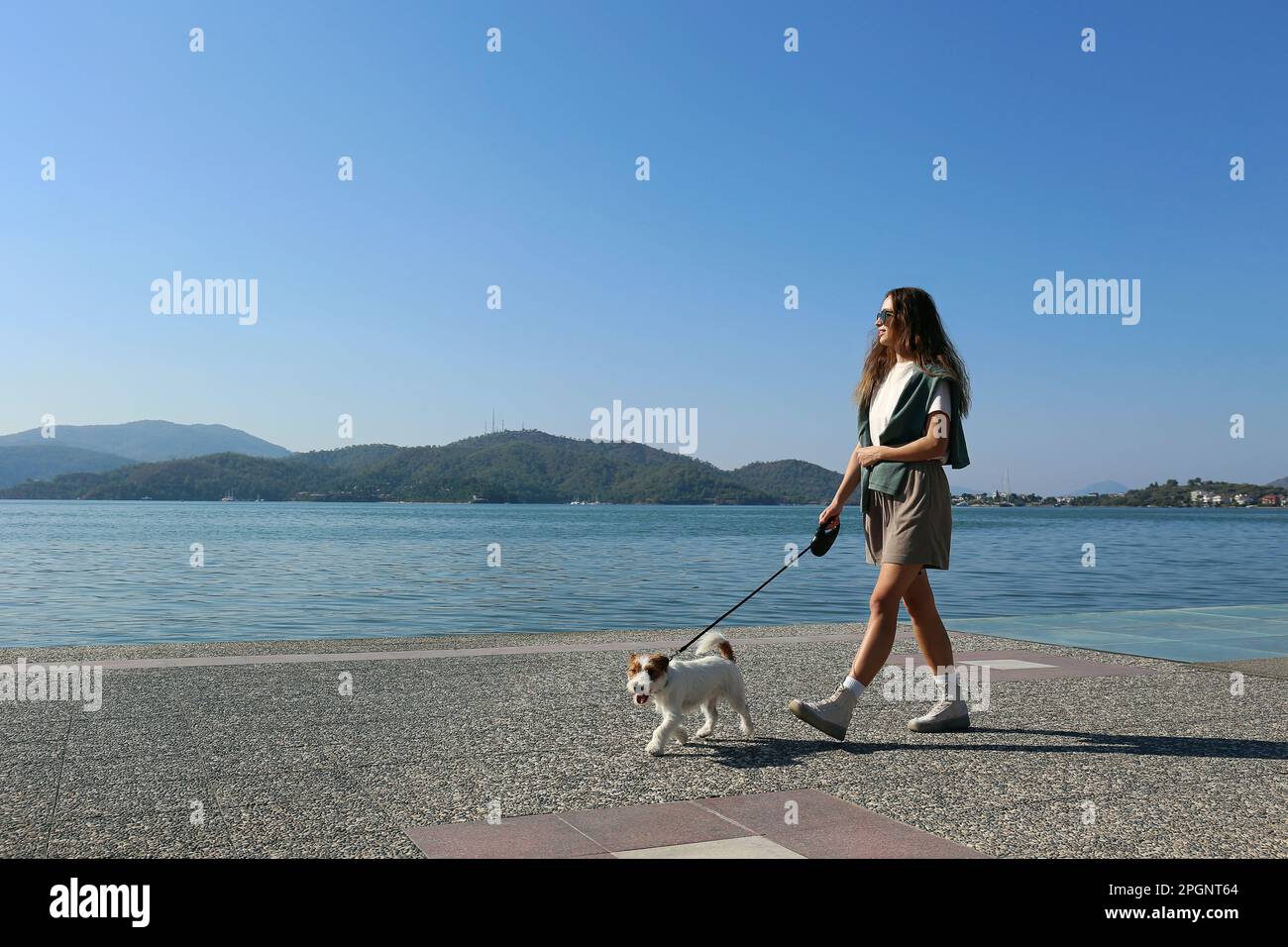 Woman walking with dog at promenade on sunny day Stock Photo