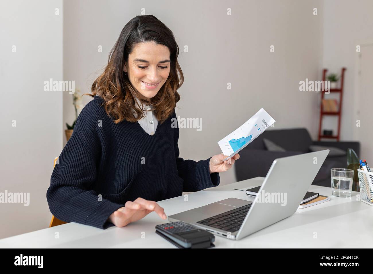 Businesswoman with document using calculator at desk Stock Photo