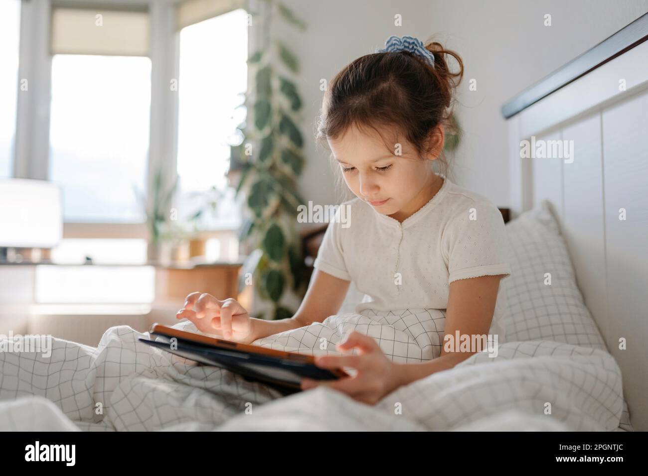 Girl using tablet PC sitting in bedroom Stock Photo