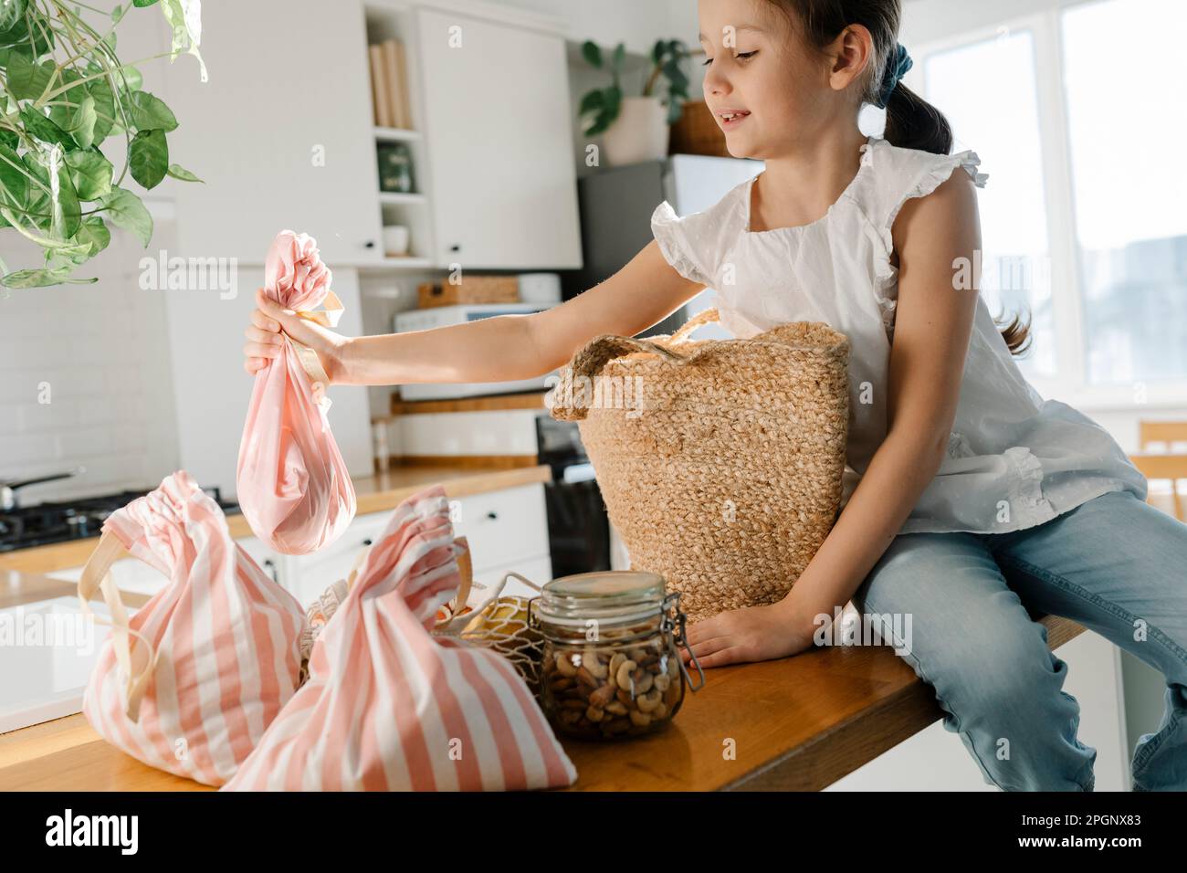 Girl with reusable bags sitting on kitchen island Stock Photo