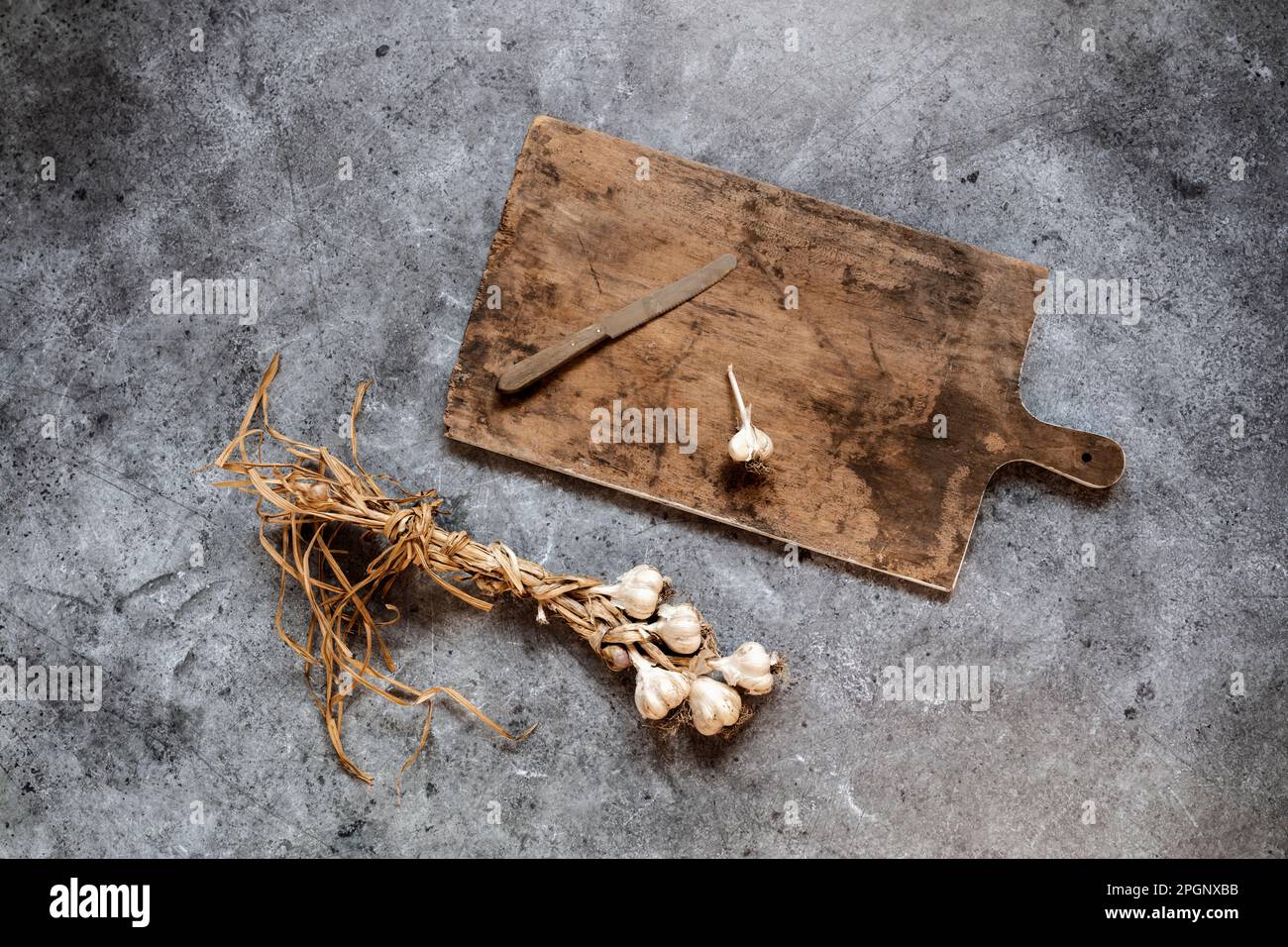 Raw garlic, cutting board and kitchen knife lying on gray surface Stock Photo