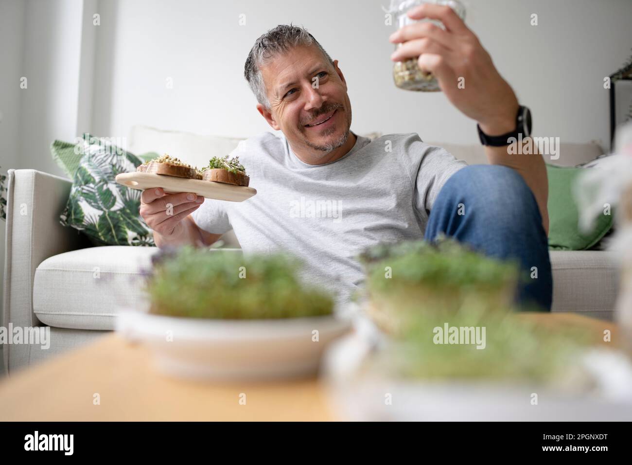 Happy man holding sprouts jar in living room at home Stock Photo