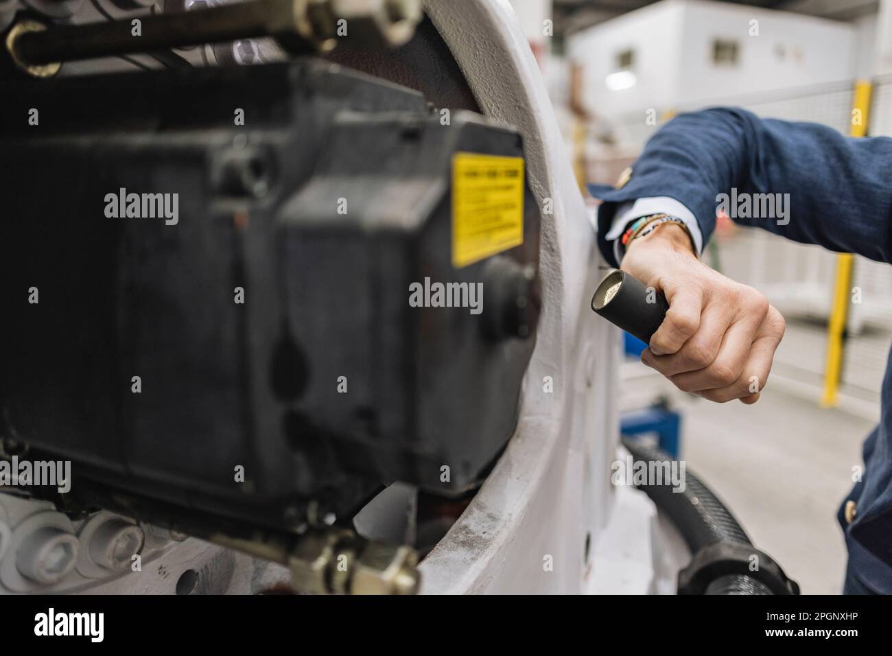 Hand of engineer holding flashlight examining machine part in factory Stock Photo