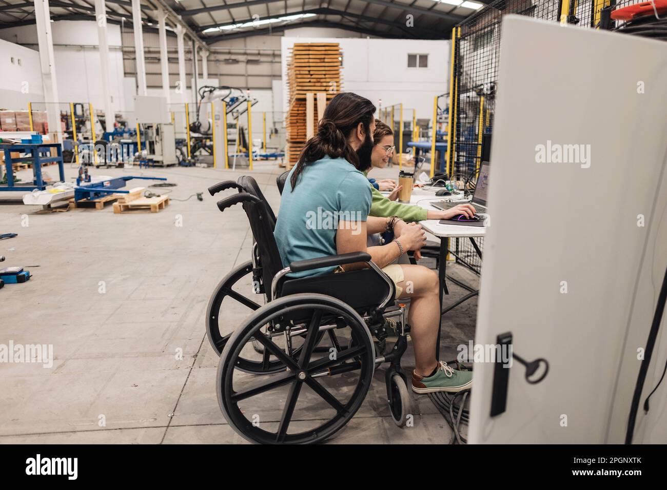 Engineer sitting in wheelchair working with colleague in factory Stock