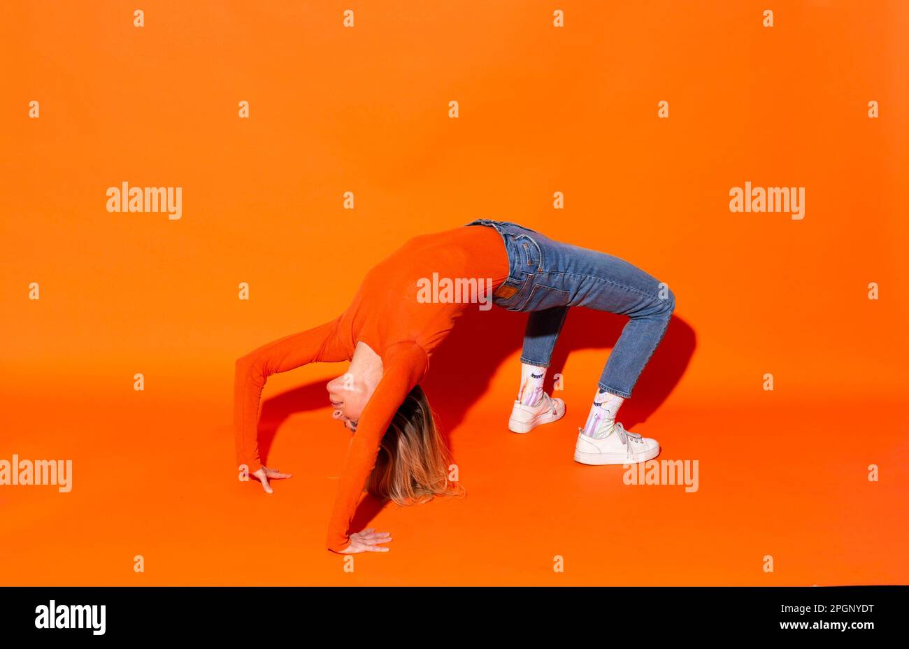 Woman making bridge position against orange background Stock Photo