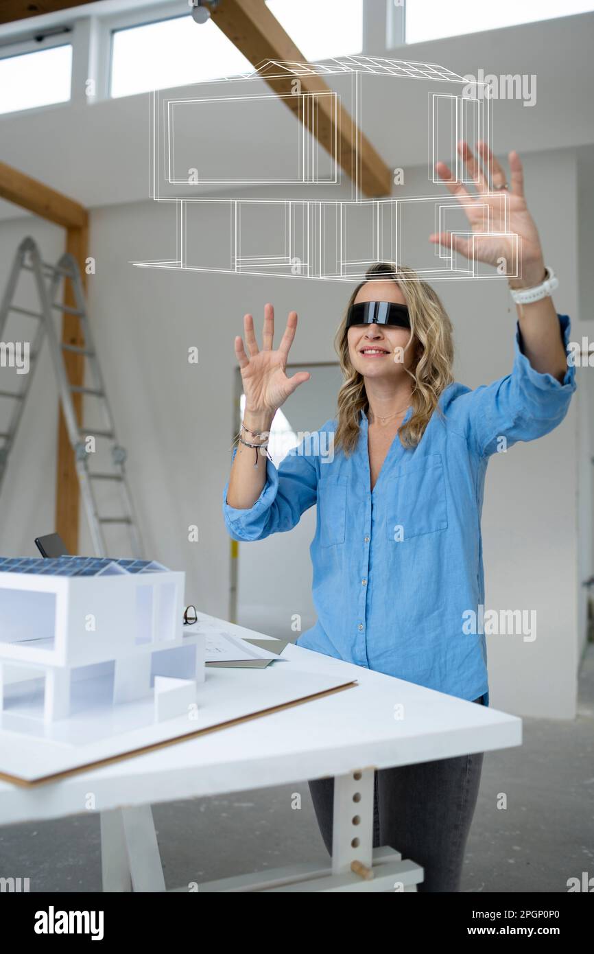 Smiling architect wearing virtual reality simulator examining house model over table Stock Photo