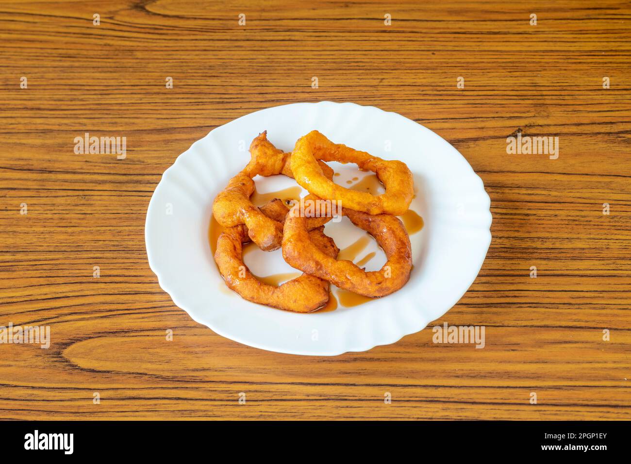 Picarones are ring-shaped fried sweets made with wheat flour dough mixed with squash, and sometimes sweet potato, bathed in flavored chancaca honey Stock Photo