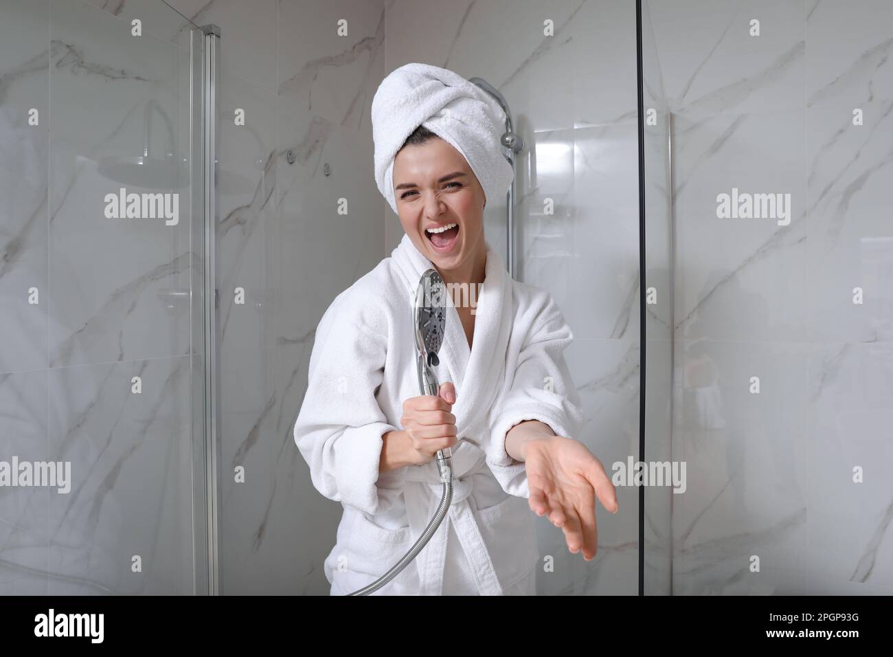 Beautiful young woman singing into showerhead in bathroom Stock Photo