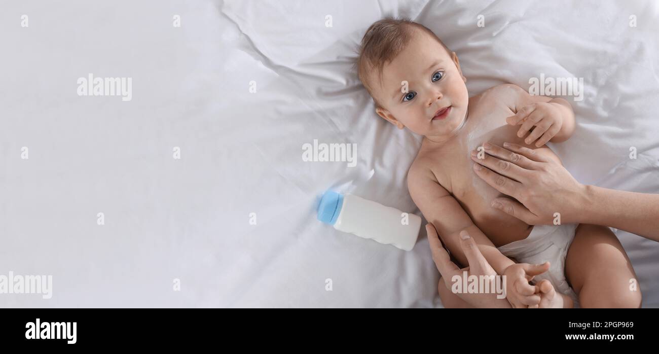 Mother applying dusting powder onto her baby on bed, top view with ...