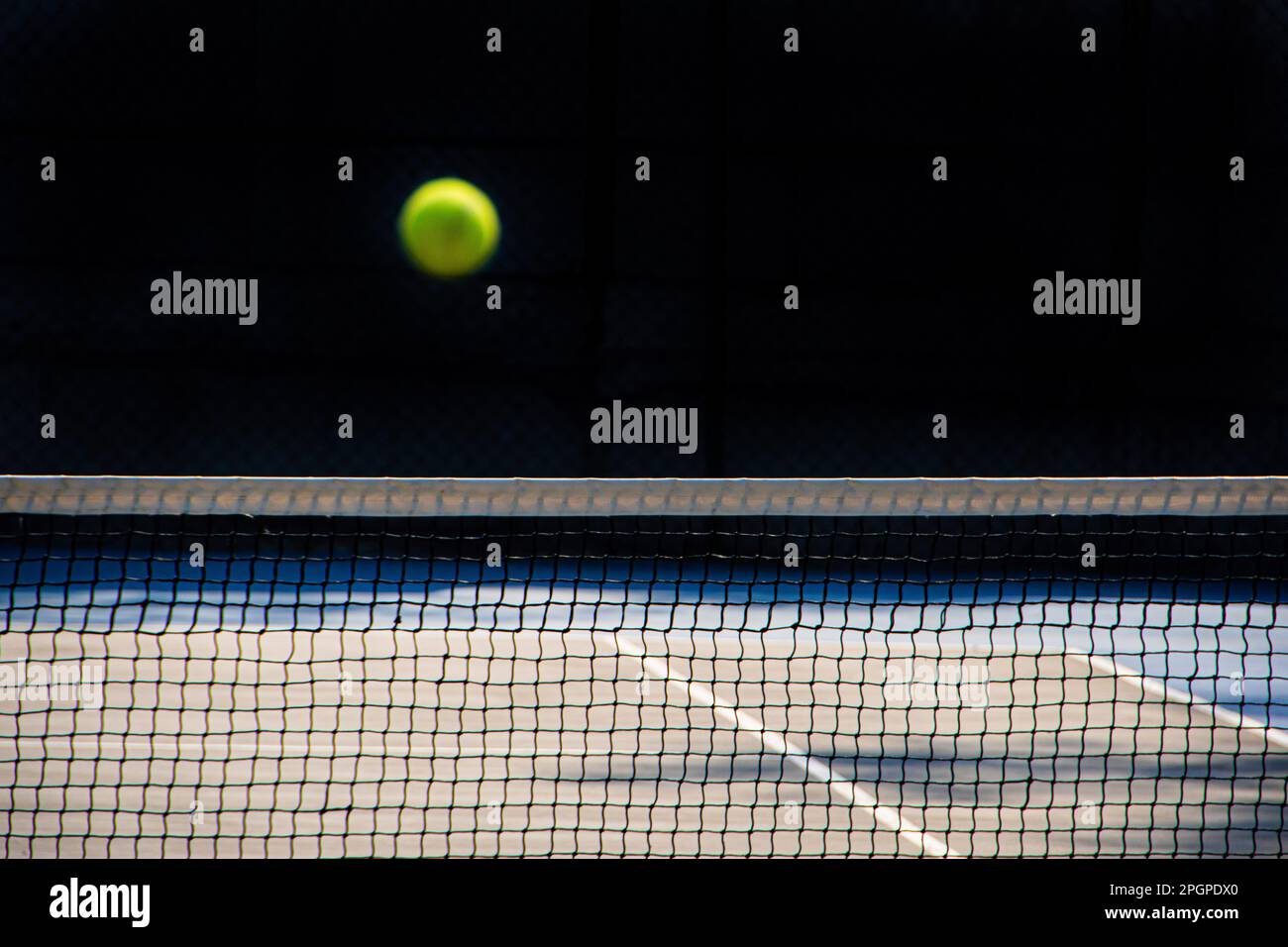 Tennis ball out of focus crossing the net on hard court. Black