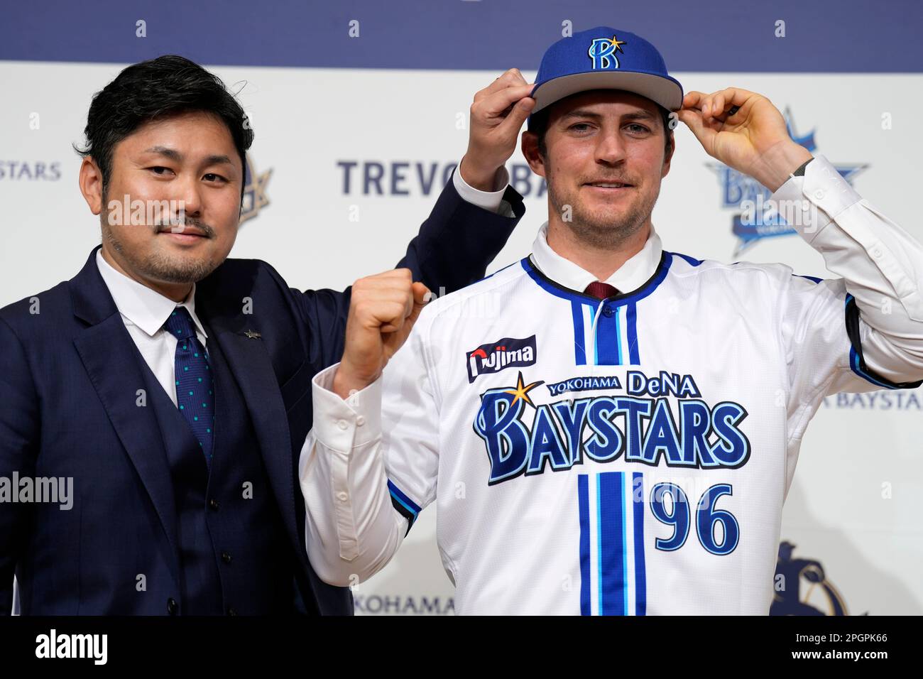 Trevor Bauer shows his new uniform and cap of Yokohama DeNA BayStars with  Tatsuhiro Hagiwara, left, senior director of Team Operations Department  during a photo session of the news conference Friday, March