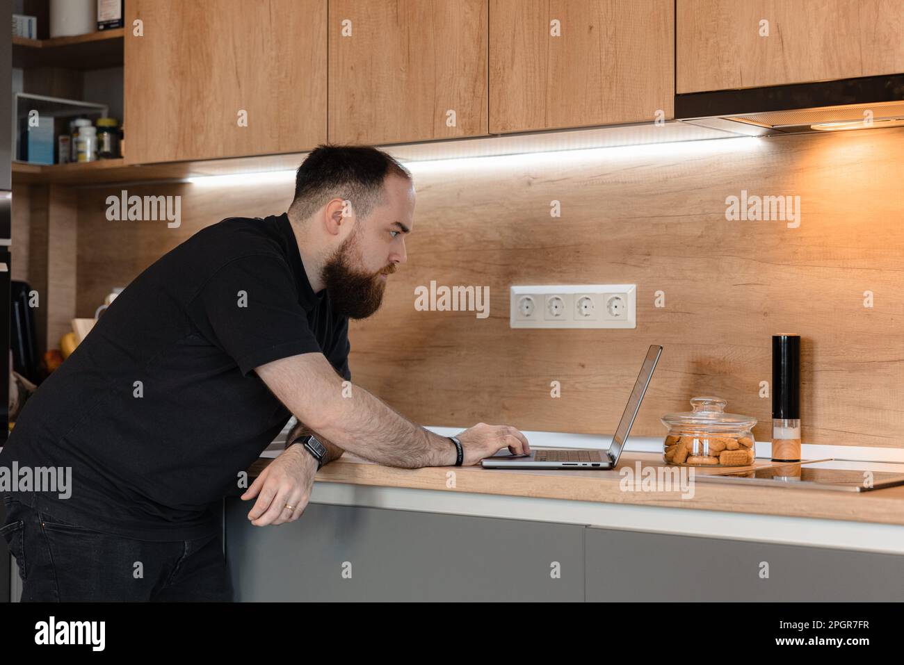 A man is sitting at his modern kitchen counter, typing away on his ...