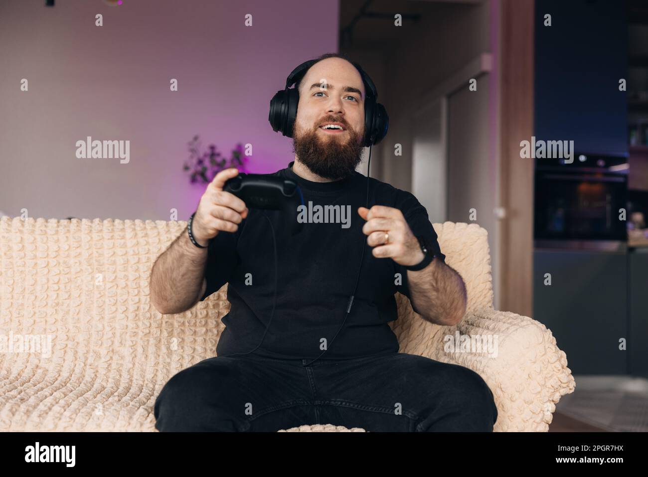 Male gamer playing video games with the controller in his hands and his headsets on. Face expression of a gamer. Stock Photo