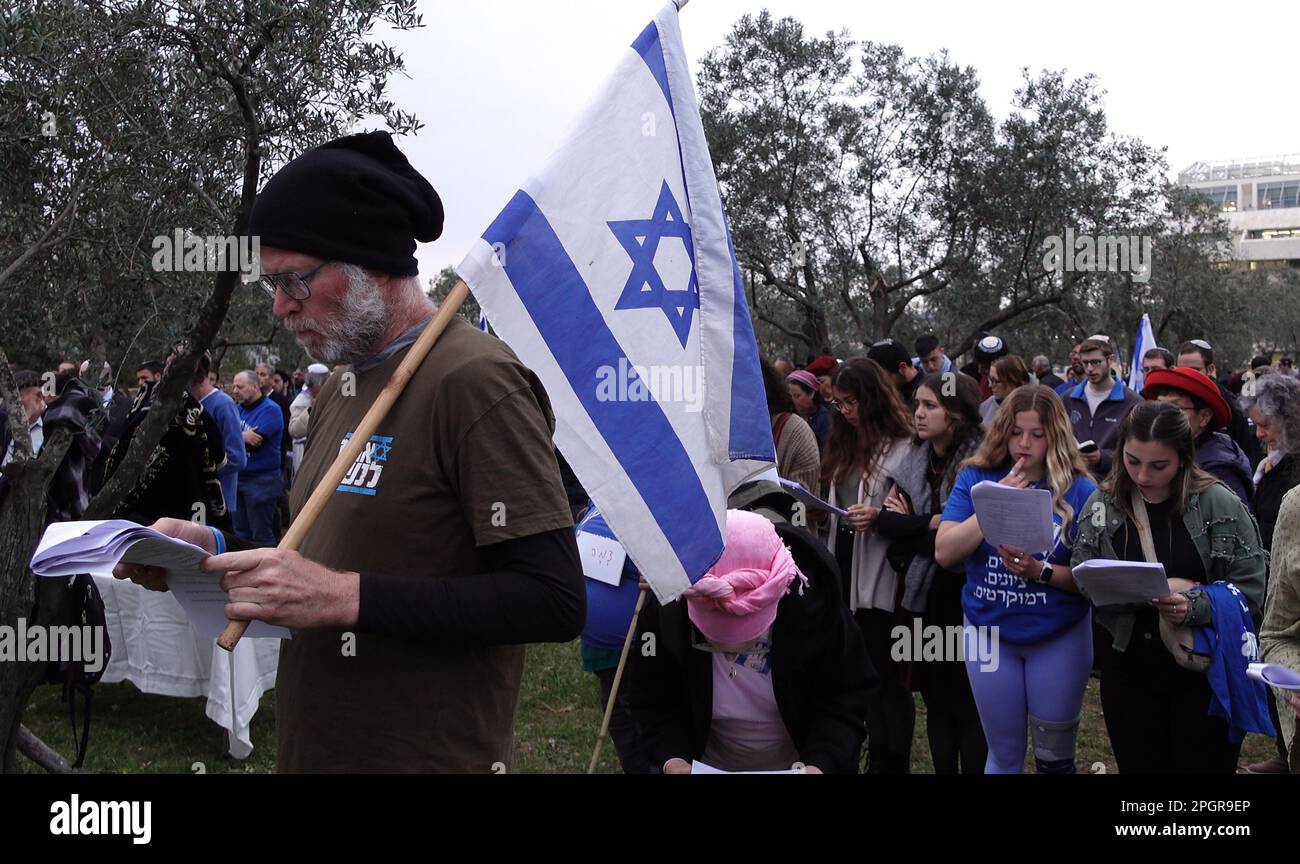 Anti government protester holding an Israeli flag joins a prayer held by religious Jews in a plea for unity and divine deliverance from rising tensions over the country’s judicial overhaul in front of the Israeli Supreme court on March 22, 2023 in Jerusalem, Israel. The Netanyahu government is pushing ahead with proposed overhaul of the judiciary that would limit the Israeli Supreme Court's ability to review and strike down laws that it deems unconstitutional. Stock Photo