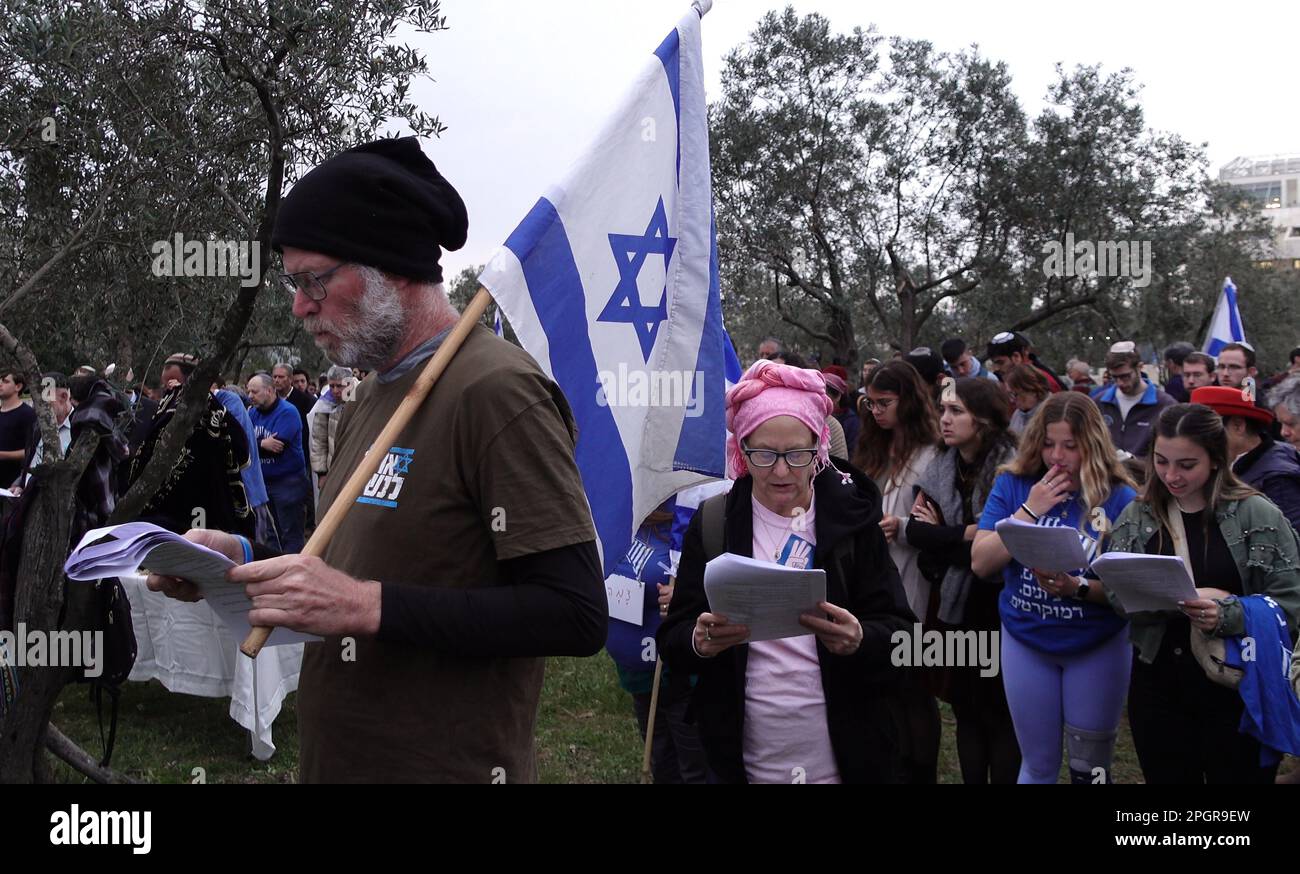 Anti government protester holding an Israeli flag joins a prayer held by religious Jews in a plea for unity and divine deliverance from rising tensions over the country’s judicial overhaul in front of the Israeli Supreme court on March 22, 2023 in Jerusalem, Israel. The Netanyahu government is pushing ahead with proposed overhaul of the judiciary that would limit the Israeli Supreme Court's ability to review and strike down laws that it deems unconstitutional. Stock Photo