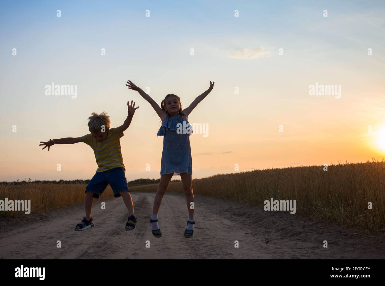 Silhouettes of cheerful girls and boys jumping for joy against the backdrop of the sunset sky. fun, excitement. childhood, summer walks, friendship Stock Photo