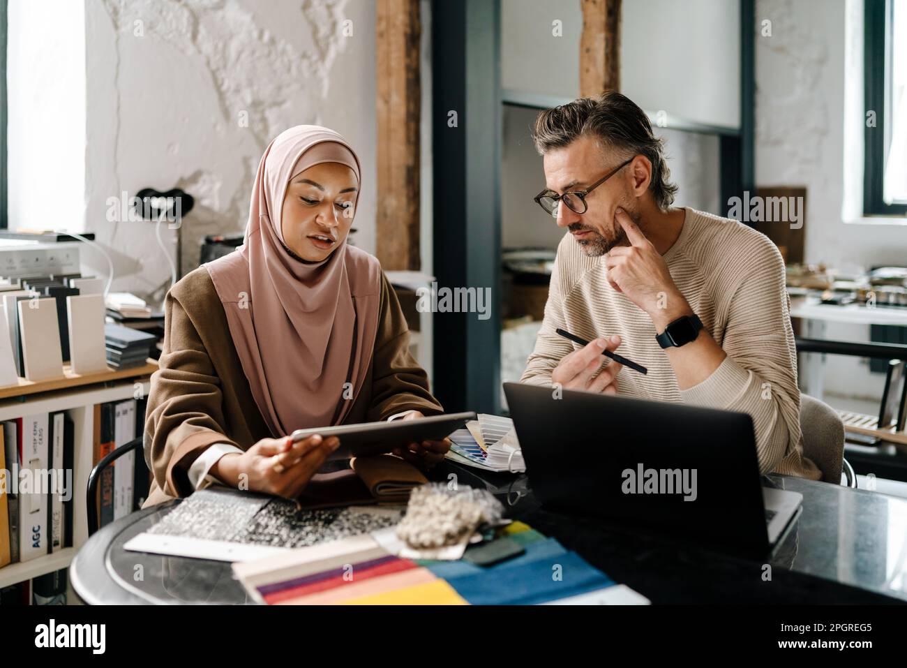 Two multinational colleagues designers working with laptop computer at workshop indoors Stock Photo