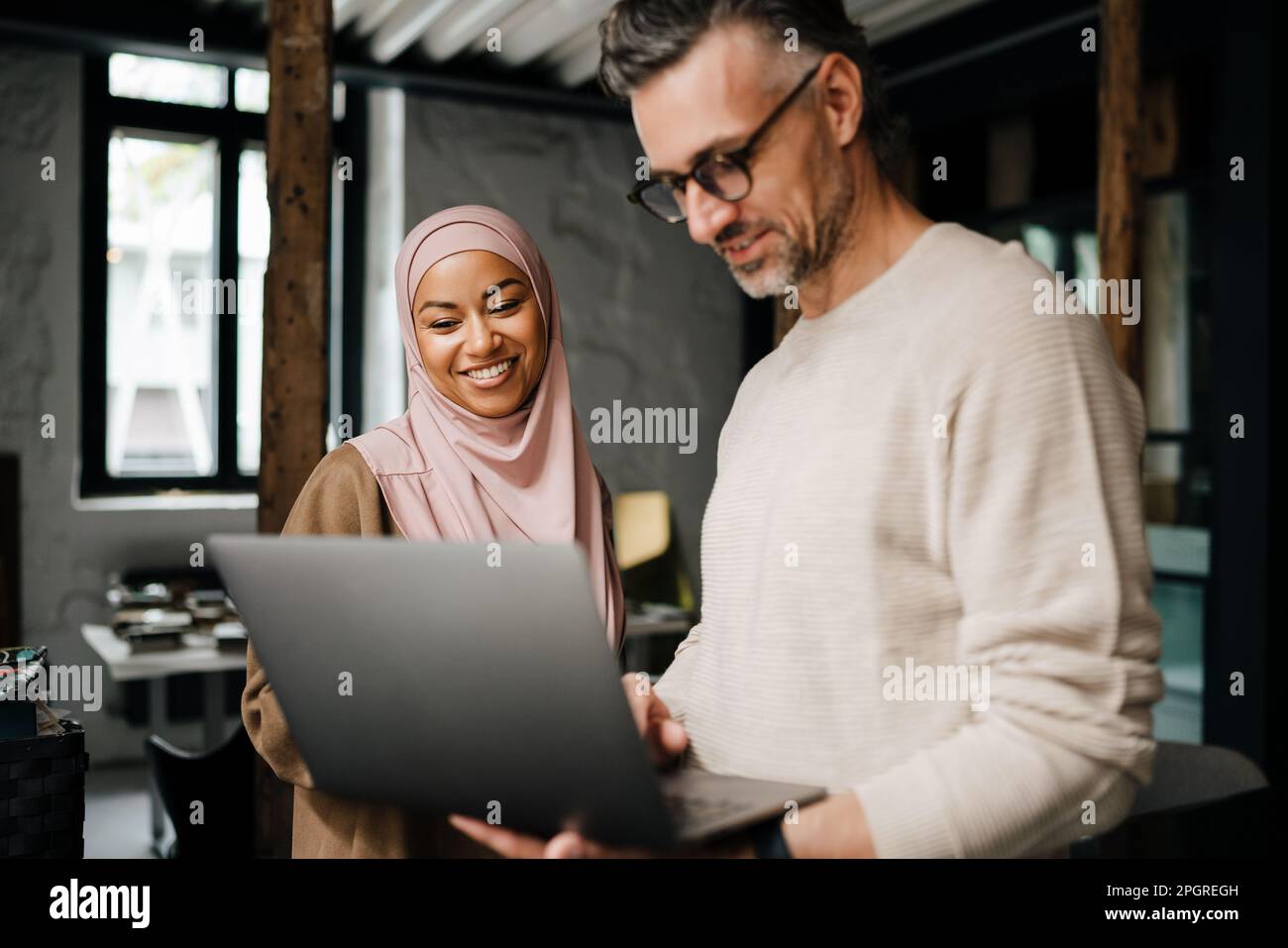 Two multinational colleagues smiling while working with laptop computer in modern office Stock Photo