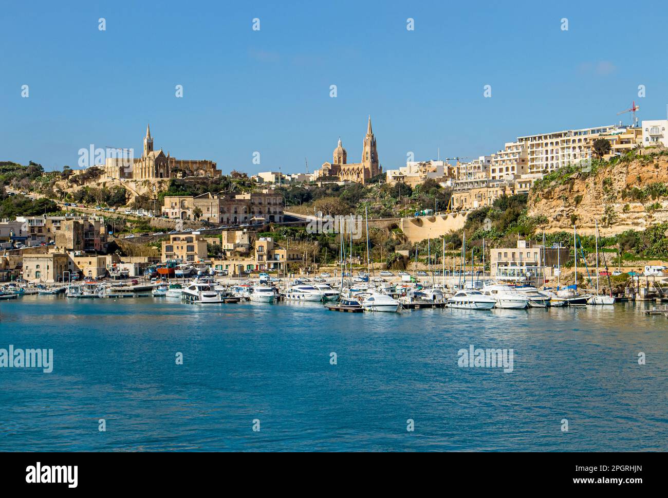 The port of Mġarr on the island of Gozo, Malta. Beautiful city on the cliffs and hills on the background on sunny spring day. Stock Photo