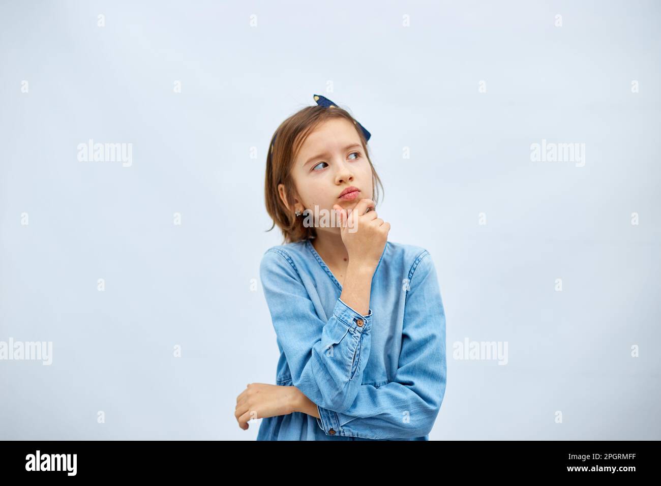 Thoughtful teen girl child wearing jeans dress with finger thinking or considering, have an idea in studio on white background, making decision imagin Stock Photo