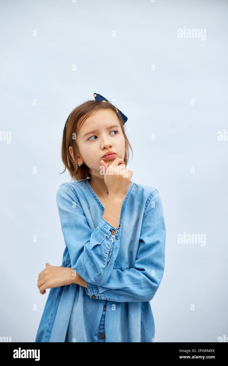 Thoughtful teen girl child wearing jeans dress with finger thinking or considering, have an idea in studio on white background, making decision imagin Stock Photo