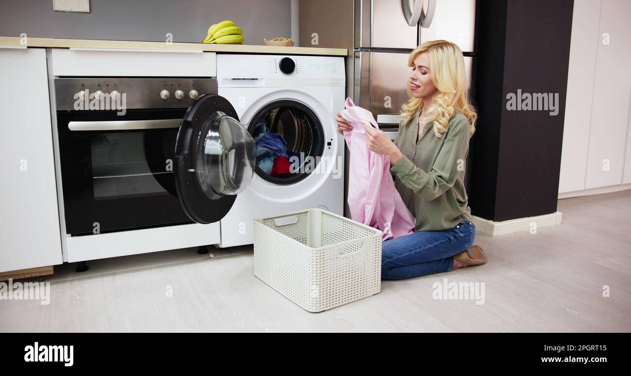 Woman Smelling Clean Clothes Near The Electronic Washer At Laundry Room Stock Photo