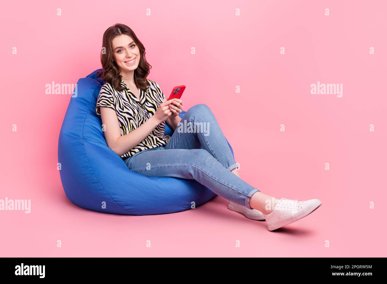 Full body photo of attractive girl sit bean bag hold smartphone curly brown hair customer review website interface isolated on pink color background Stock Photo