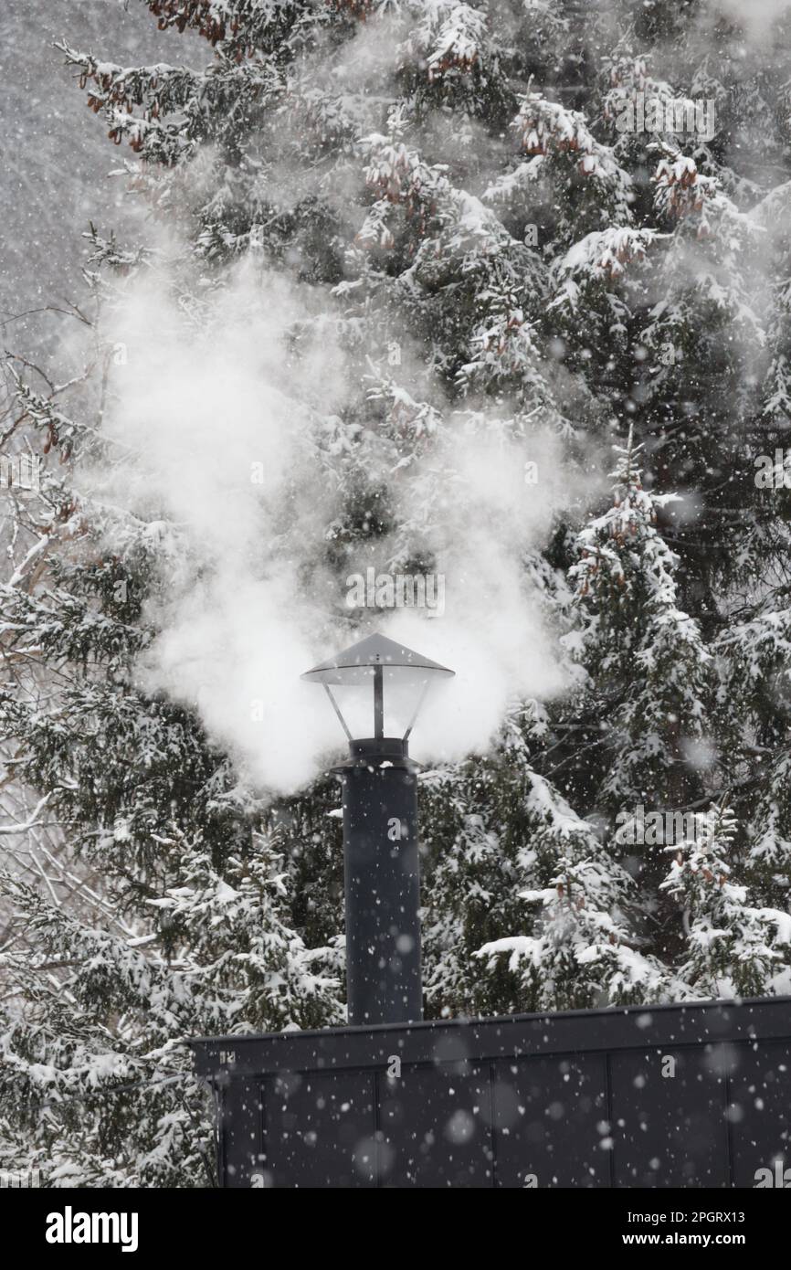 White smoke and black metal chimney on a snowy day Stock Photo
