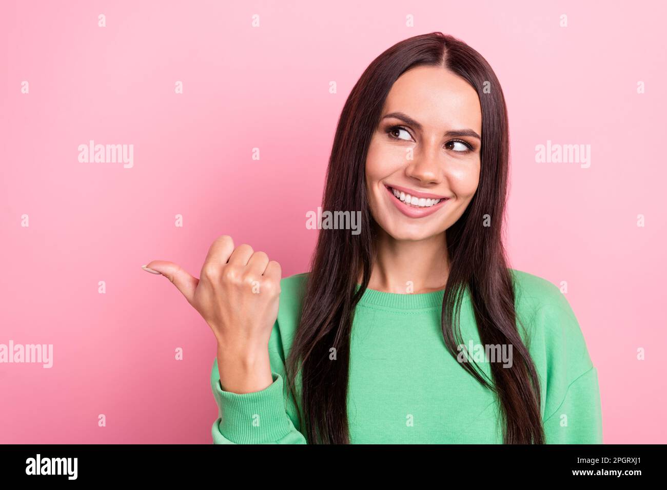 Closeup photo of young smiling pretty woman wear stylish green shirt look point thumb mockup new discount offer isolated on pink color background Stock Photo