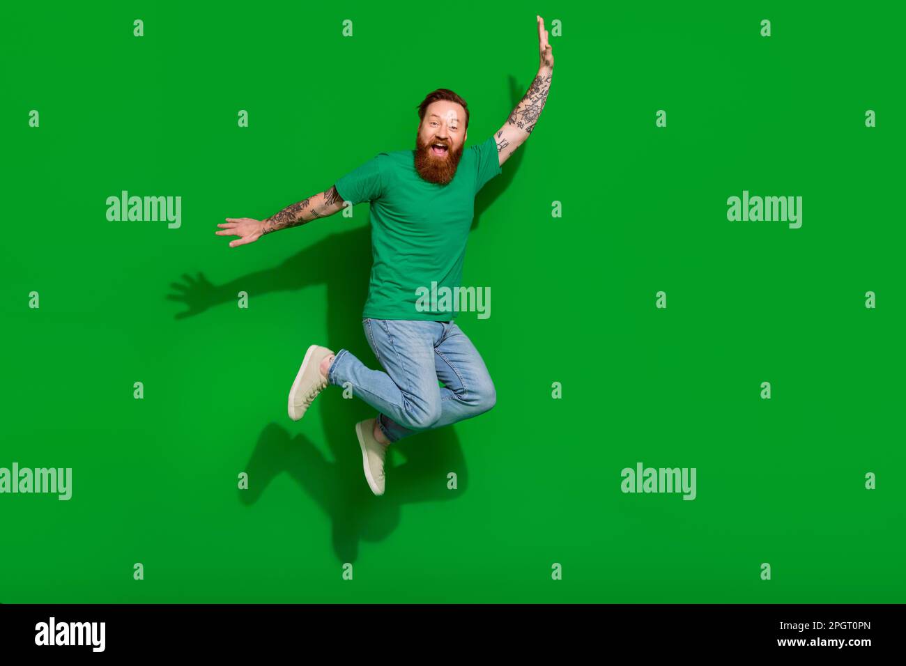 Full size photo of handsome groomed childish man wear trendy t-shirt jeans jumping flying having fun isolated on green color background Stock Photo