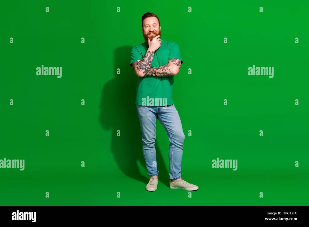 Full length photo of funky thoughtful guy dressed t-shirt arm chin smiling isolated green color background Stock Photo