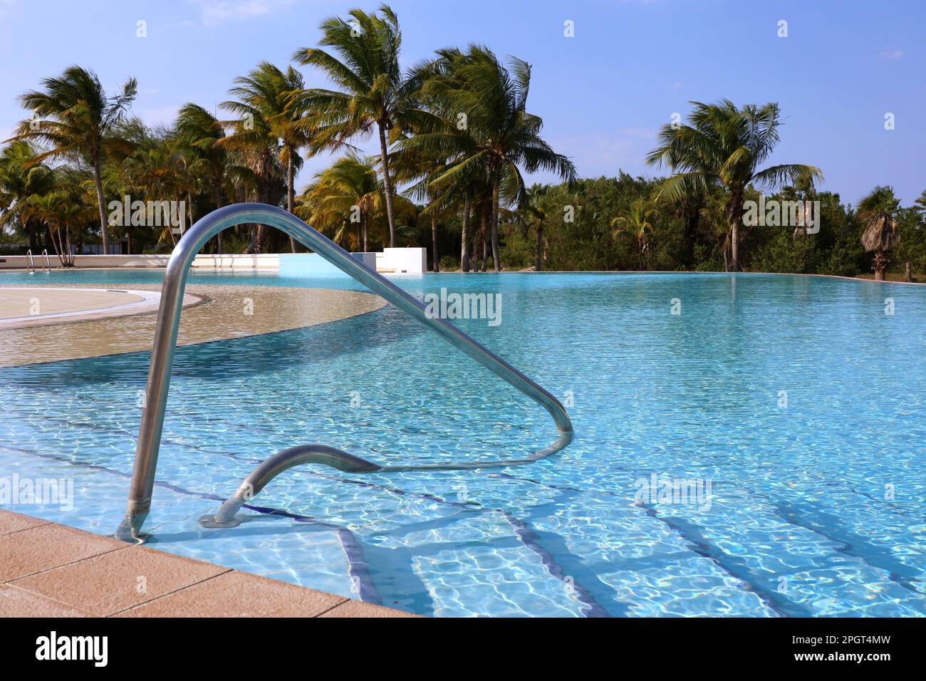 View to steps into the swimming pool with a railing against coconut palm trees. Vacation on beach resort on tropical island Stock Photo