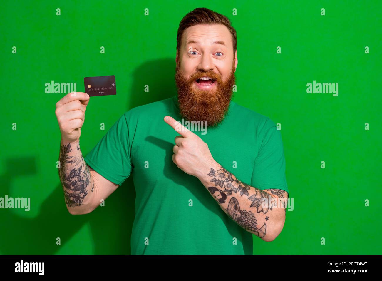 Photo of impressed astonished guy ginger beard dressed stylish t-shirt got salary on debit card isolated on green color background Stock Photo