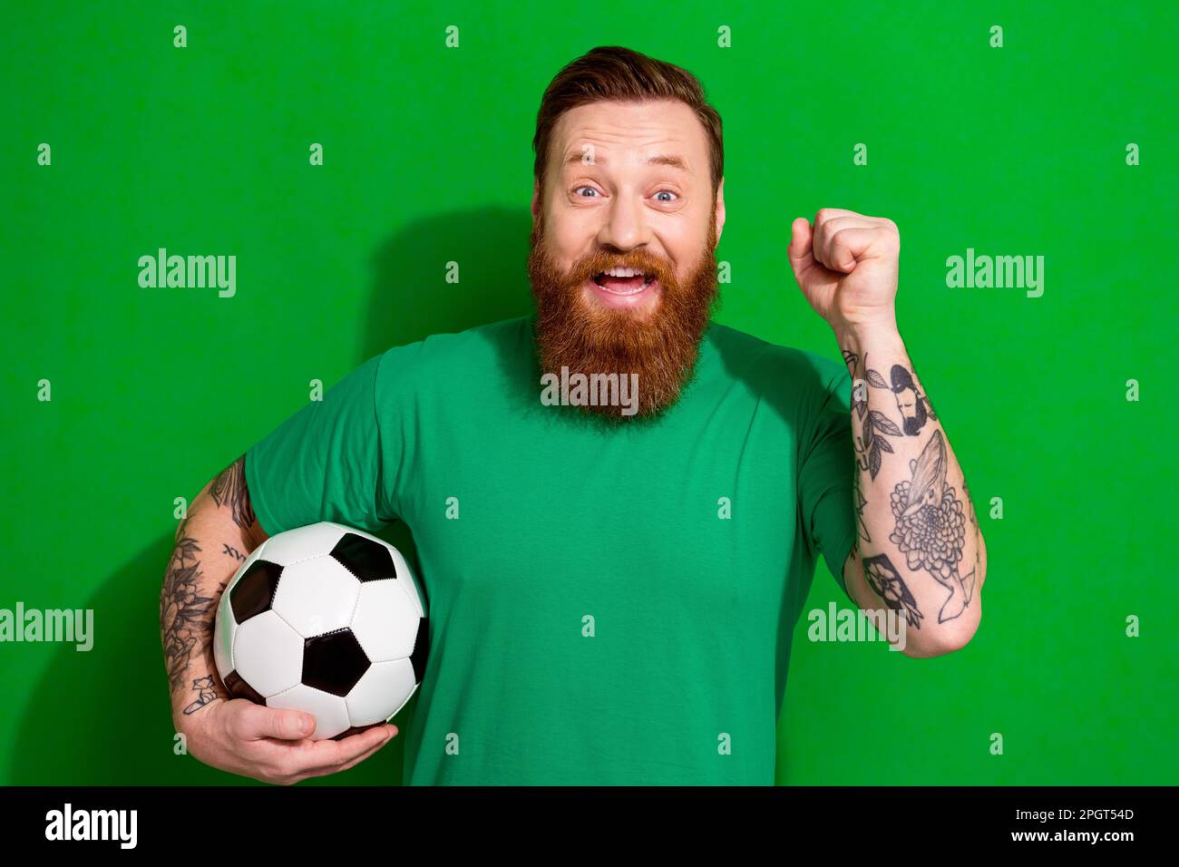 Photo of excited cheerful man wear t-shirt holding football ball rising fist isolated green color background Stock Photo