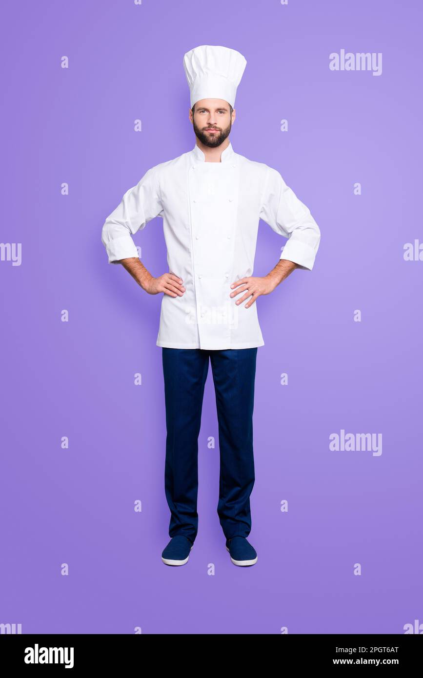 Full size fullbody portrait of attractive harsh chef cook with stubble in beret, holding arms on waist, isolated over grey background, looking at Stock Photo