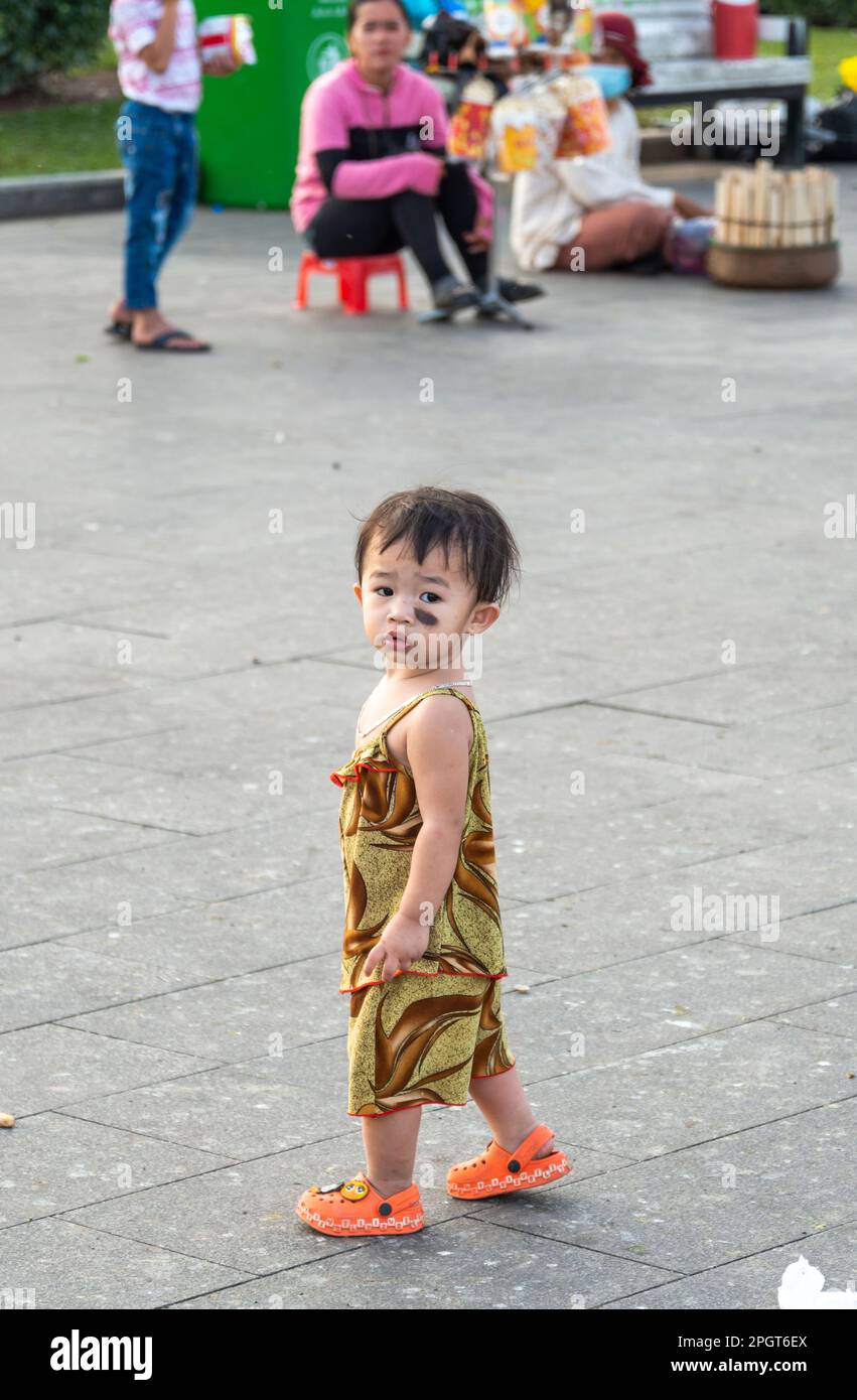 Phnom Penh,Cambodia-December 23rd 2022:A young boy,the small son of local street traders,toddles about as his Mother looks on,at Sisowath Quay,in the Stock Photo