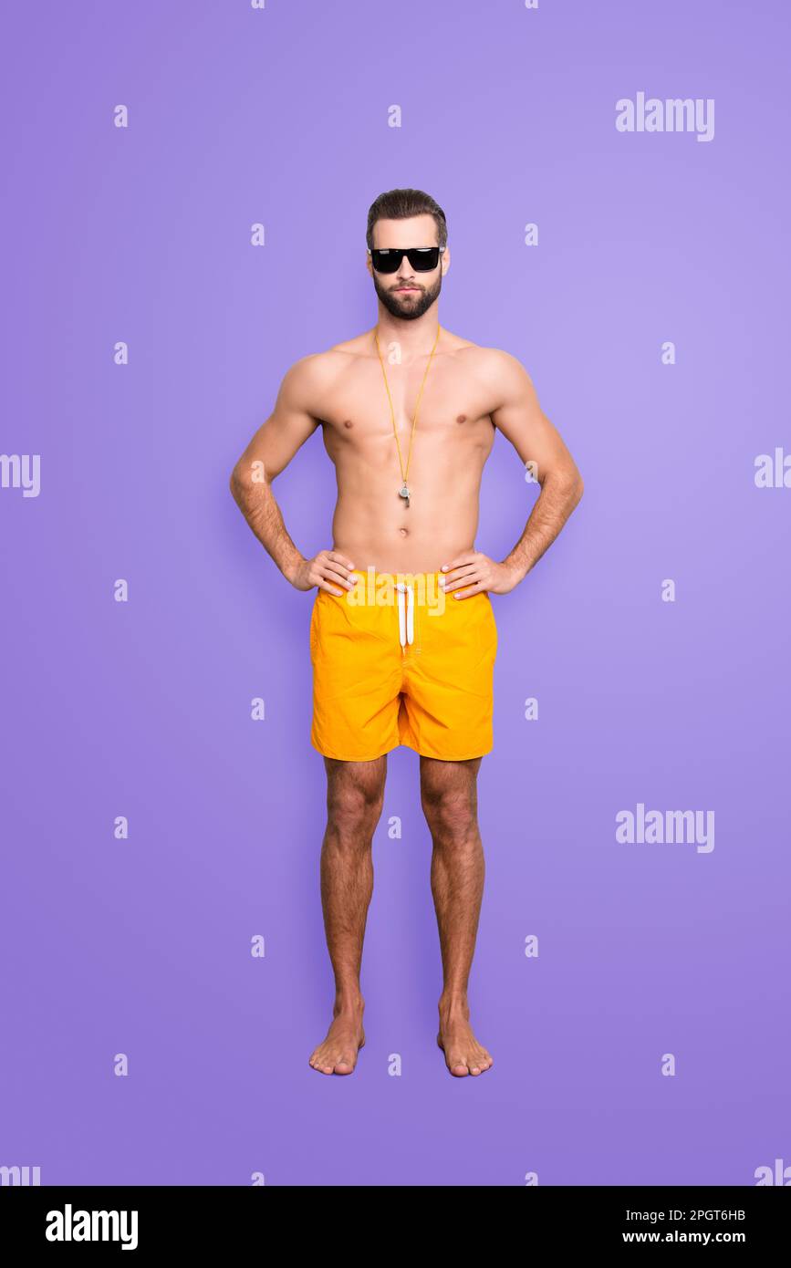 Full size body portrait of muscular athletic lifeguard with stubble in yellow shortsisolated on grey background, holding hands on waist Stock Photo