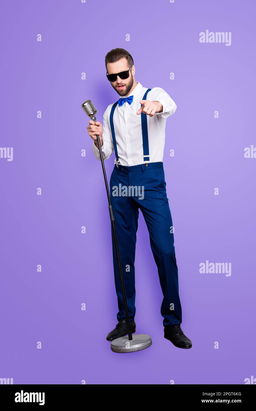 Full size fullbody portrait of handsome stylish singer in blue pants, suspenders, bow, singing hit holding mic gesture index finger front isolated on Stock Photo