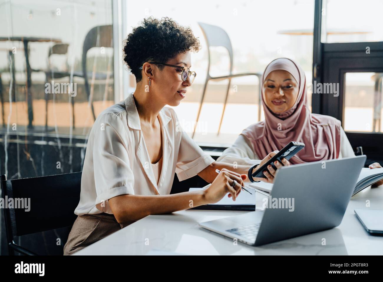 Middle-aged businesswoman and her female muslim colleague working together in office Stock Photo
