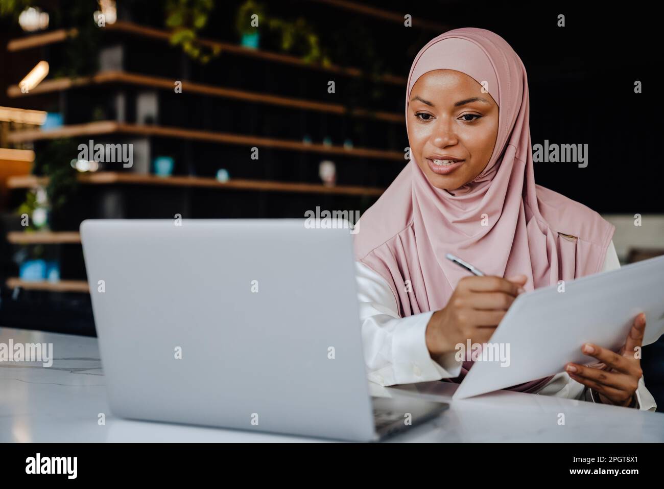 Young muslim woman wearing headscarf smiling while working on laptop in office Stock Photo