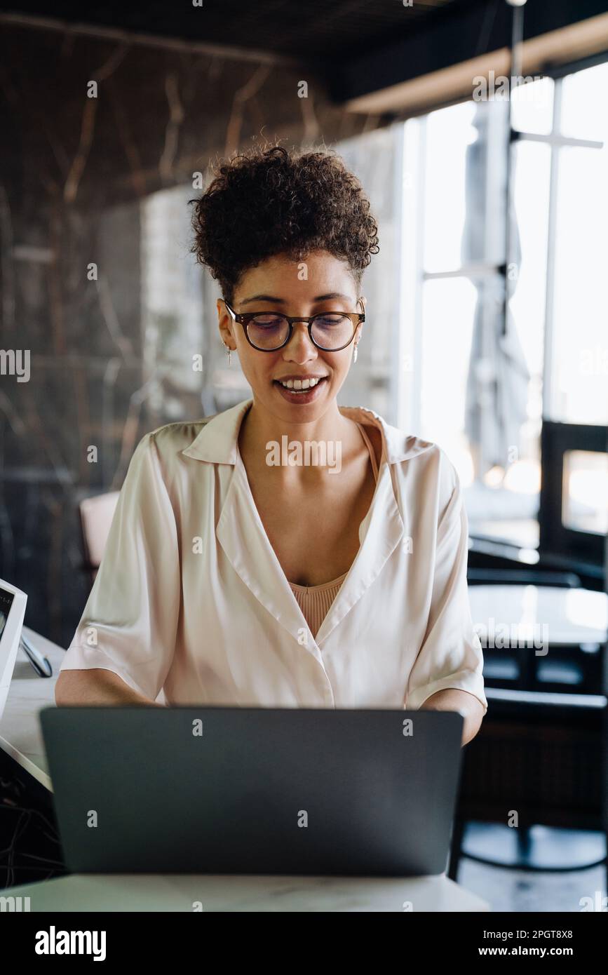 Happy black businesswoman smiling and using laptop while working in office lobby Stock Photo