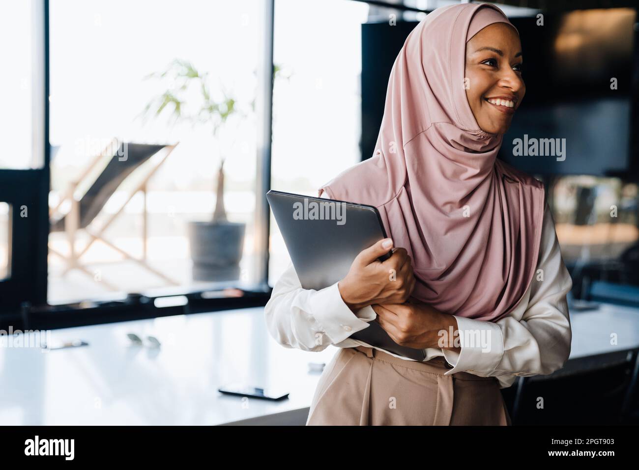 Happy muslim businesswoman smiling and holding clipboard while working in office Stock Photo