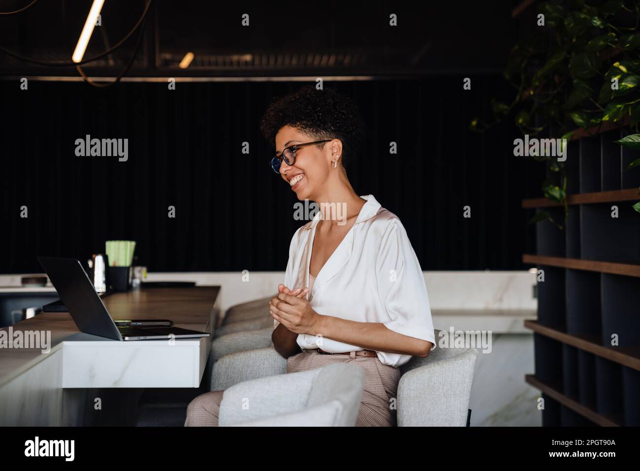 Middle-aged happy businesswoman using laptop while sitting in chair at cafe Stock Photo