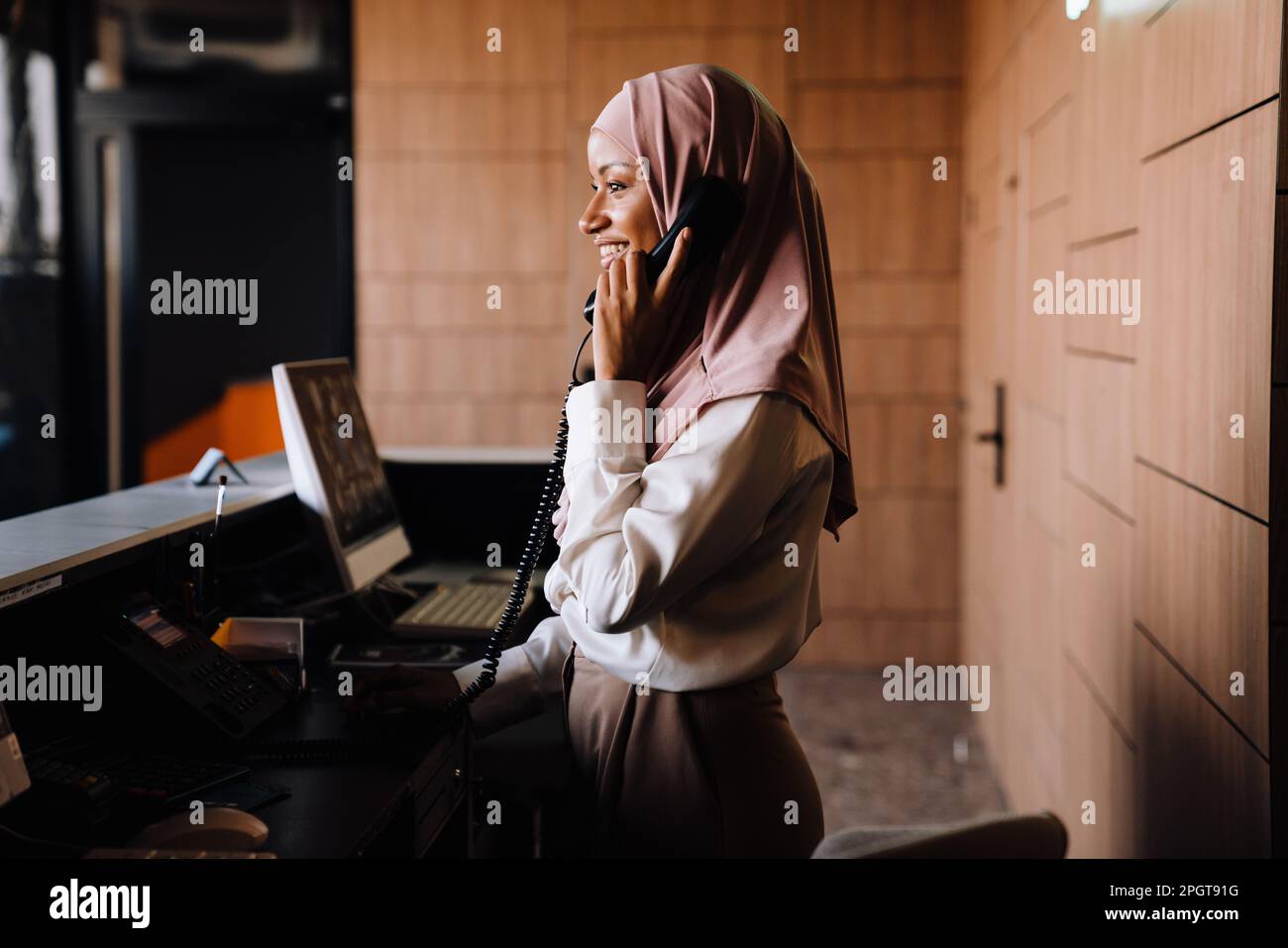 Muslim happy businesswoman talking on phone while working at reception Stock Photo